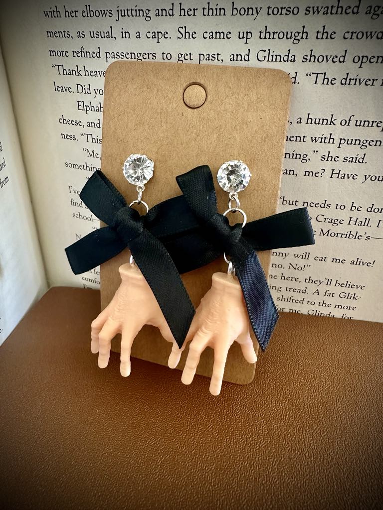 Hand-shaped earrings with black ribbons on a brown card against a book background