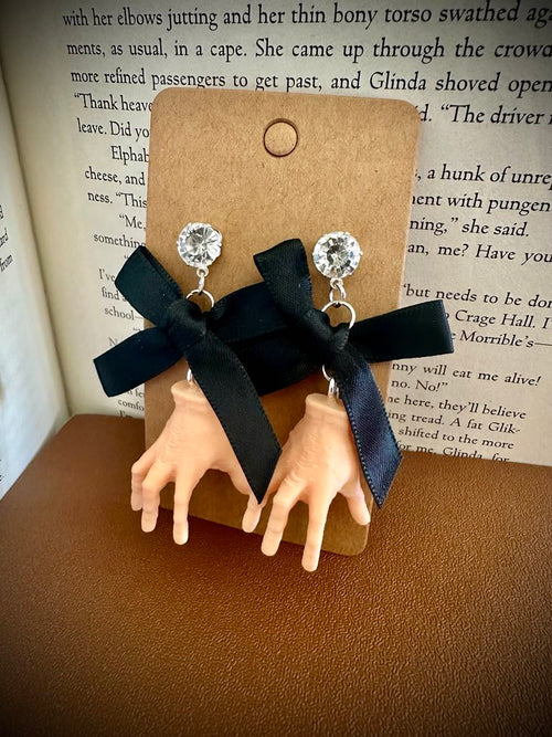 Hand-shaped earrings with black ribbons on a brown card against a book background